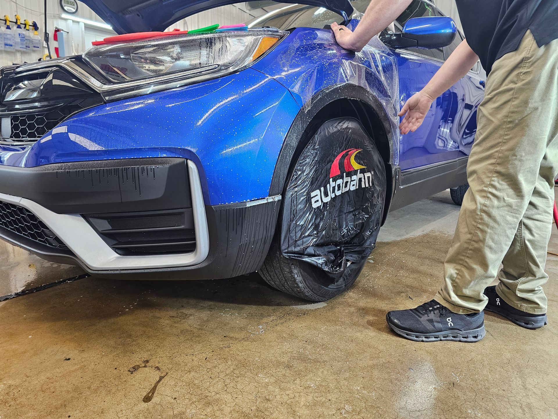 A man is wrapping a blue car with plastic wrap.