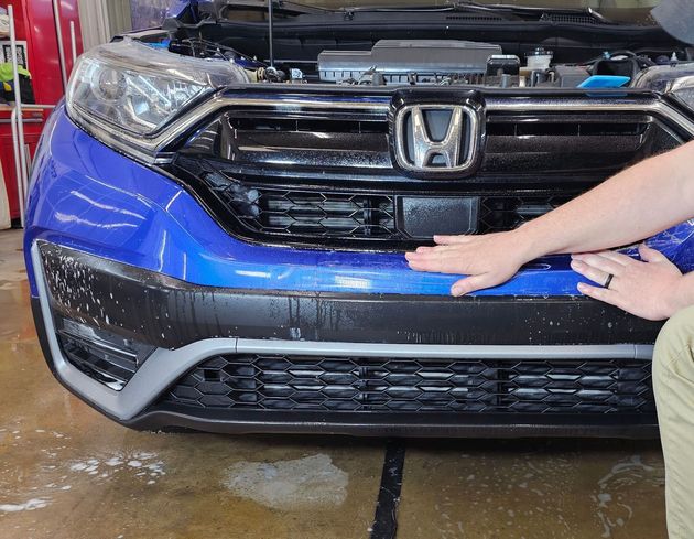 A man is touching the front of a blue honda car