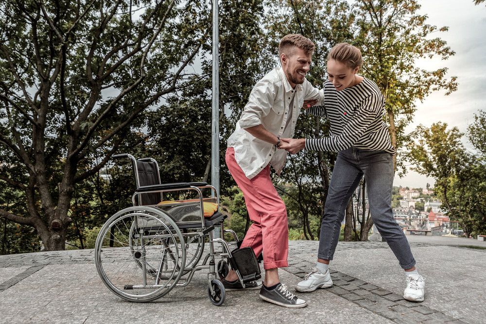 A woman helping a man in a wheelchair to stand-up.