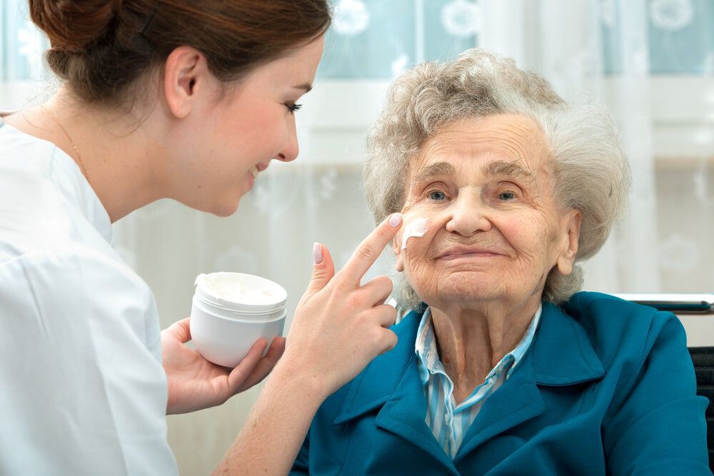 A nurse is applying cream to an elderly woman 's face.