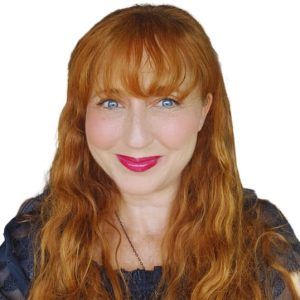 A woman with red hair and blue eyes is smiling for the camera.