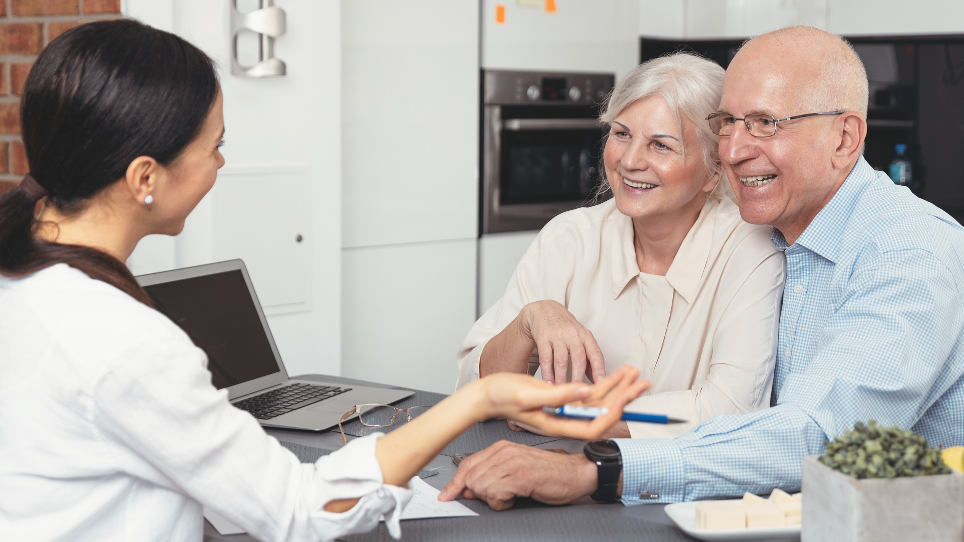 An elderly couple is sitting at a table talking to a woman.
