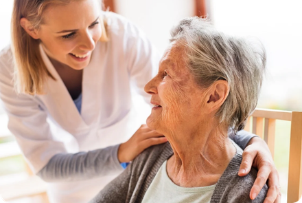 A nurse is talking to an elderly woman who is sitting in a chair.