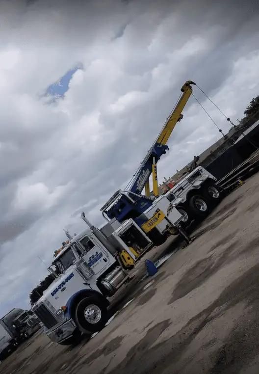 White utility truck with raised yellow crane arm parked on a wet lot under cloudy skies