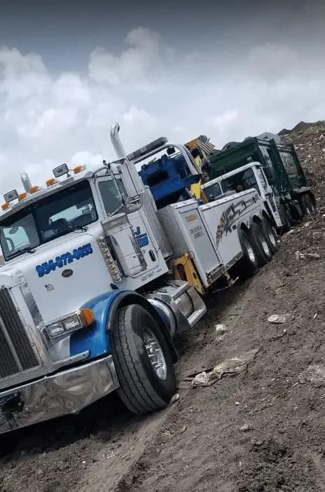 White tow truck on muddy dirt road near piles of earth under cloudy sky