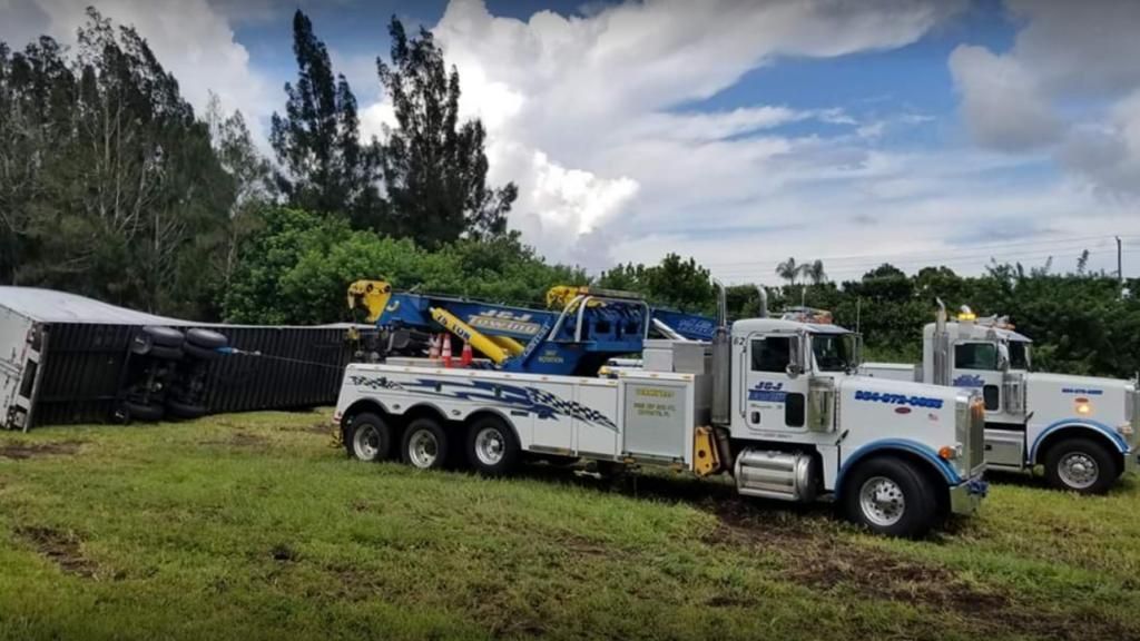 Tow trucks parked on grass beside a road under cloudy skies
