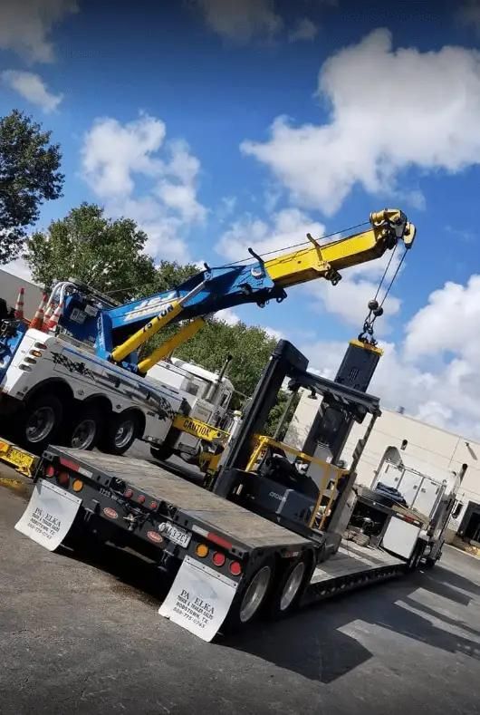 Tow truck flatbed with blue and yellow crane lifting equipment in a parking lot under a cloudy sky