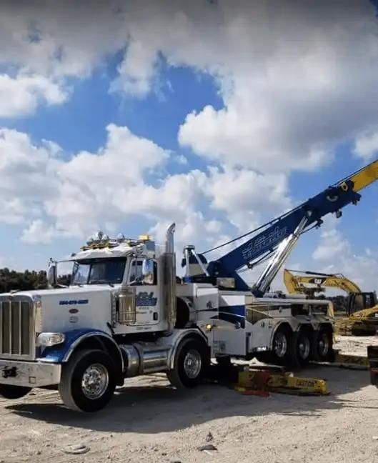 White tow truck lifting a yellow car on a lot under a partly cloudy sky