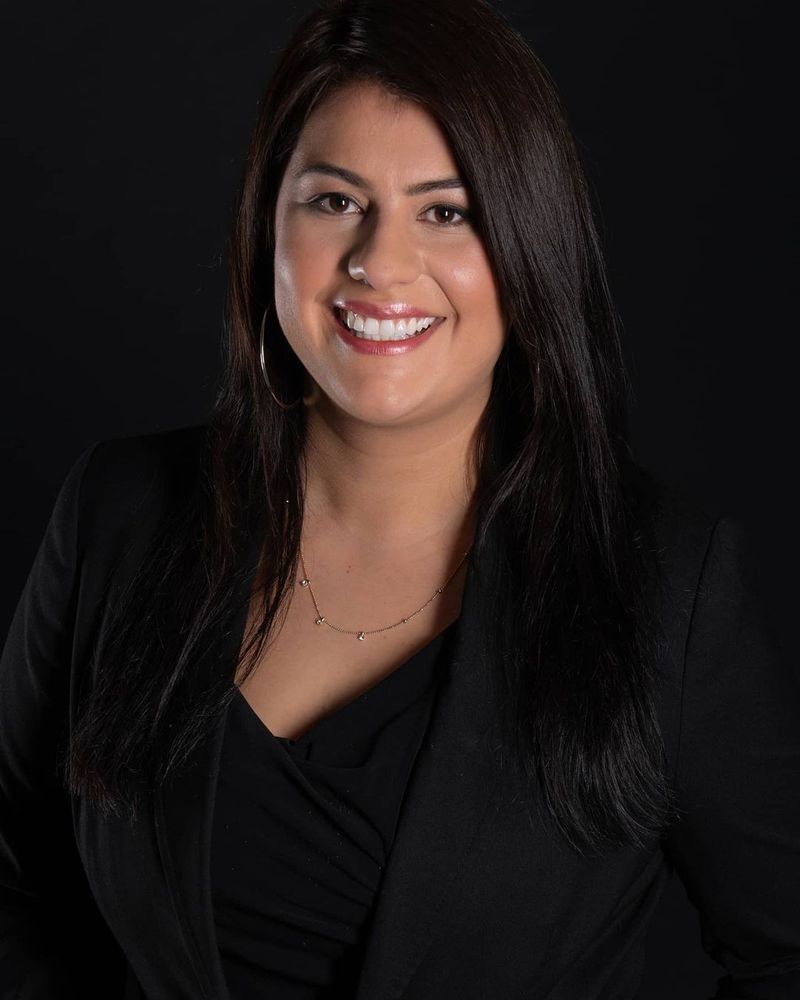 A woman is sitting at a desk with a laptop and a vase of flowers.