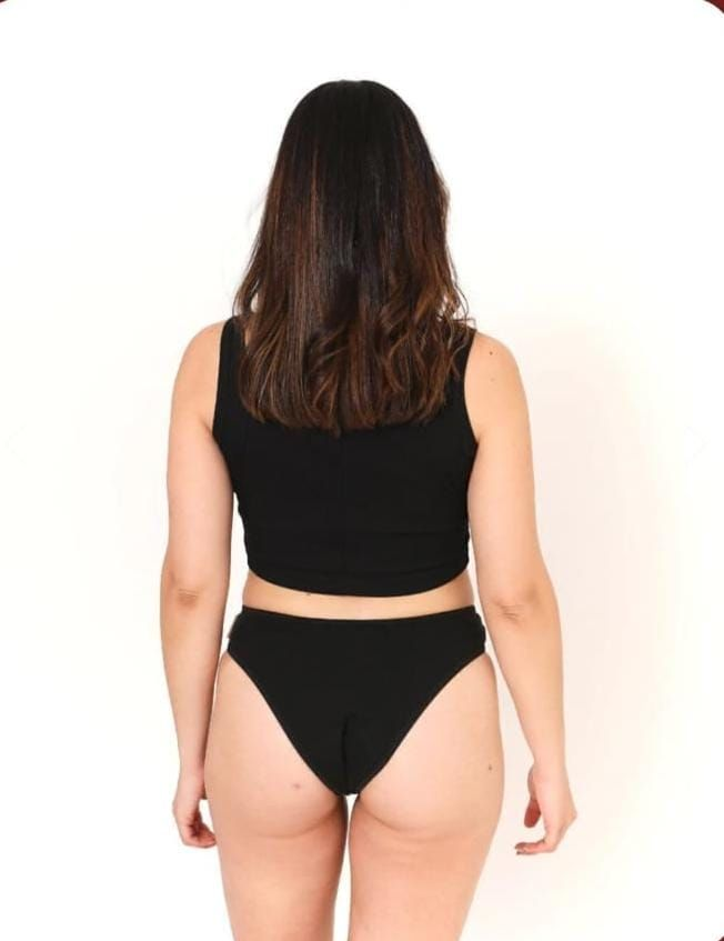 Mujer modelando un top deportivo negro y bragas de corte alto sobre un fondo blanco.
