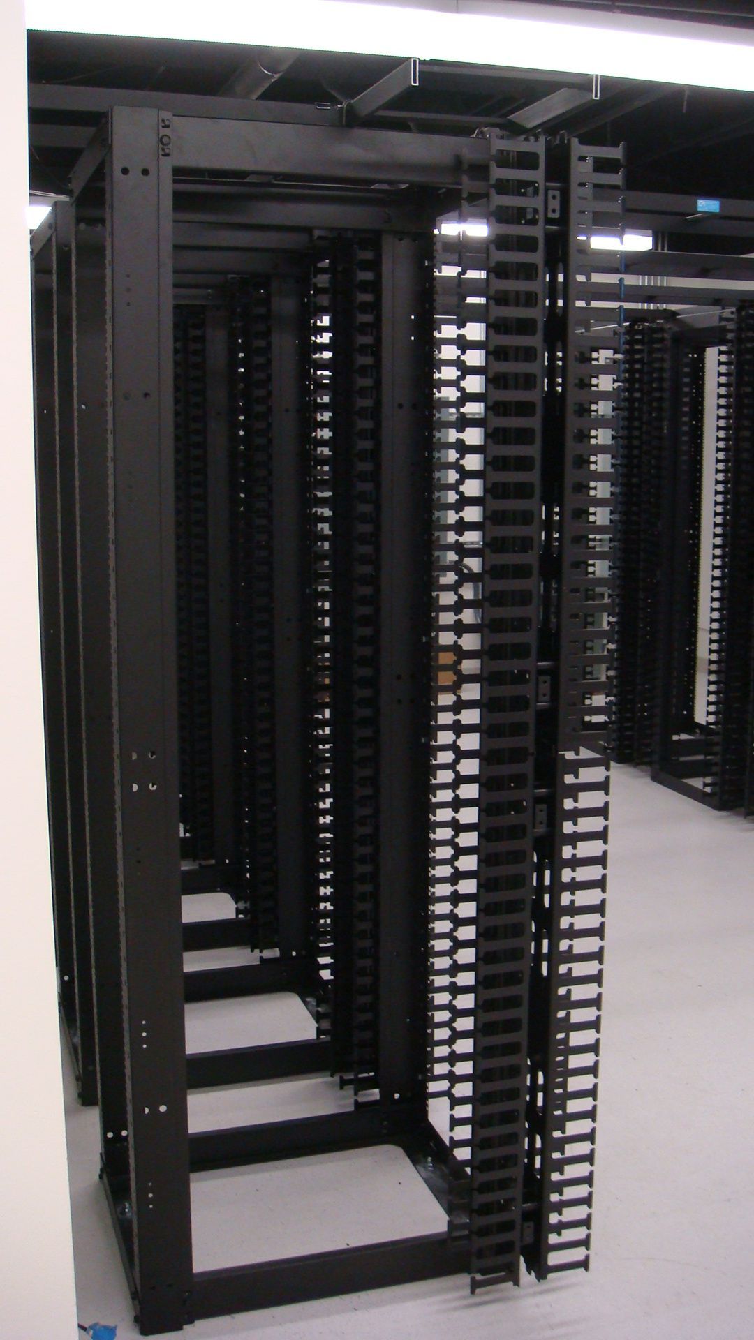 Black server racks in a data center, connected by vertical cable management.