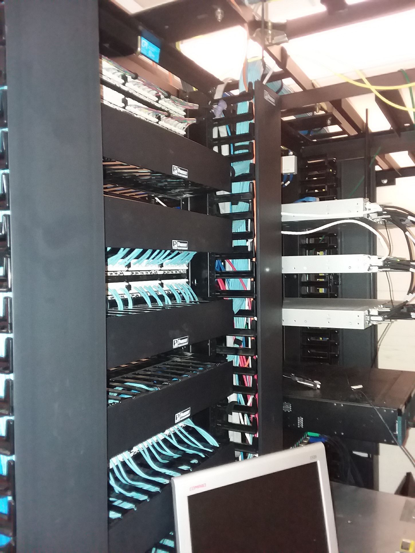 A server rack with network cables, switches, and a monitor. Black rack, blue and black cables.