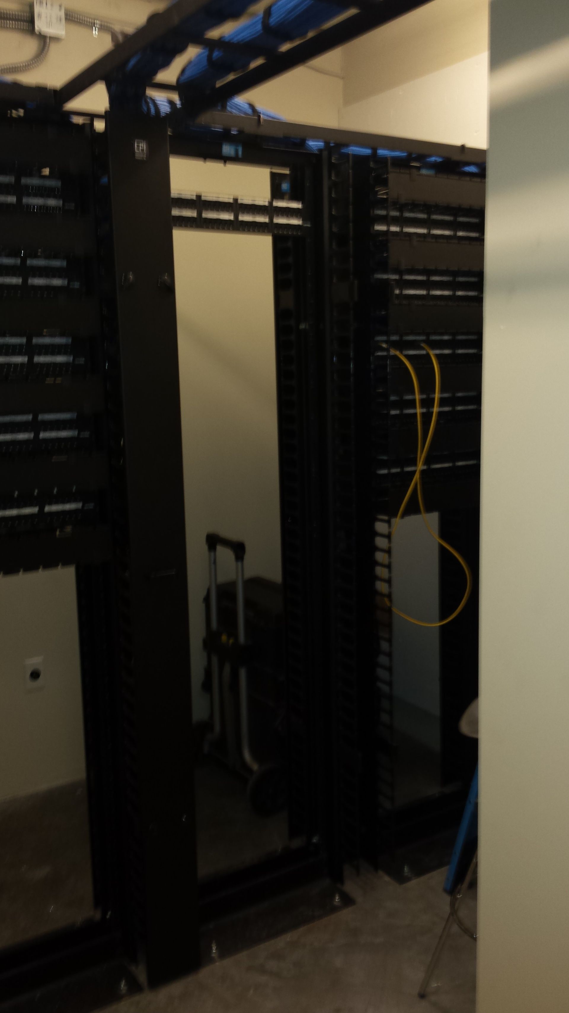 Black server racks in a room with blue and yellow cables.