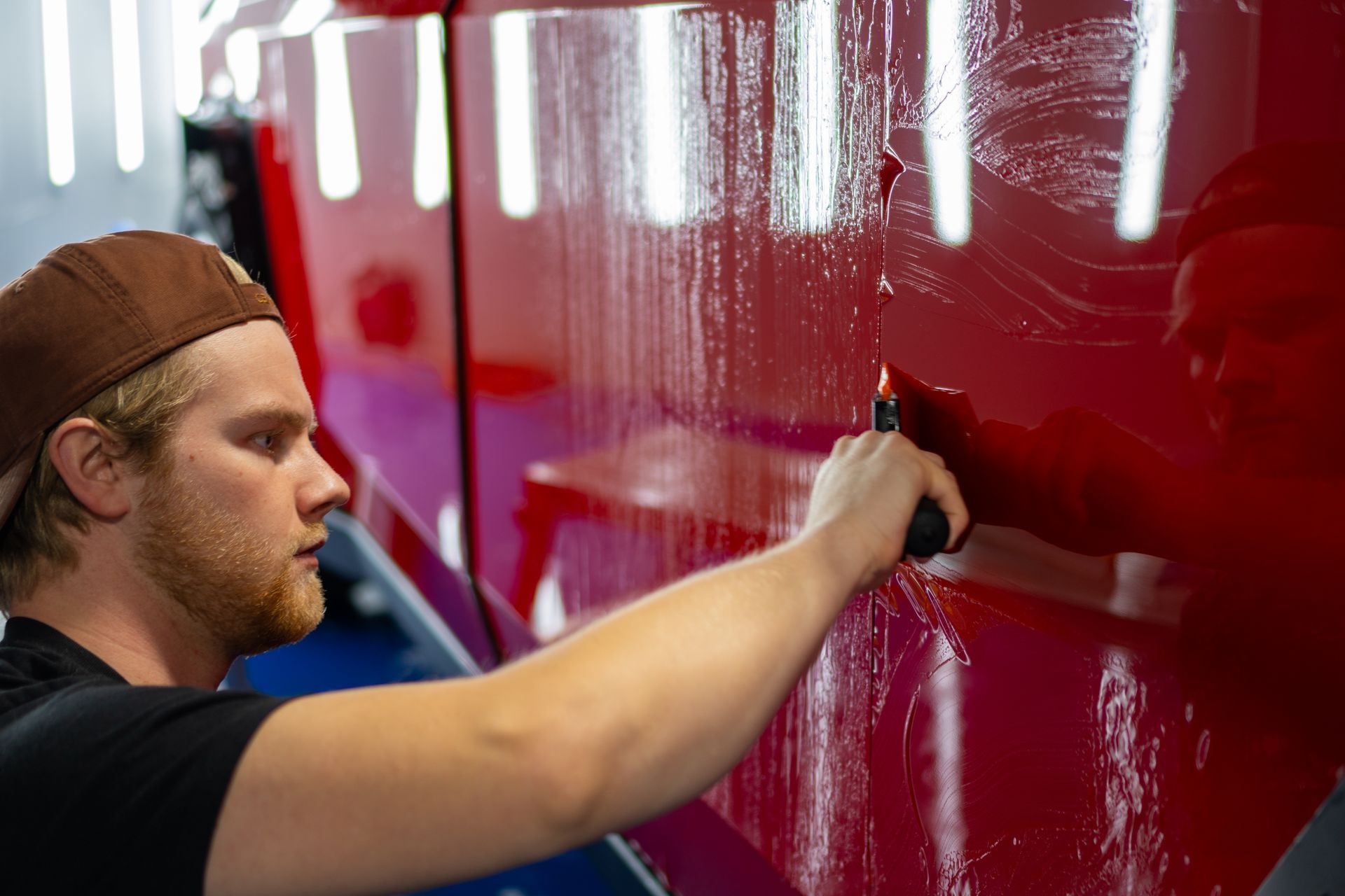Man using a knife on red car panel, presumably applying protective film.