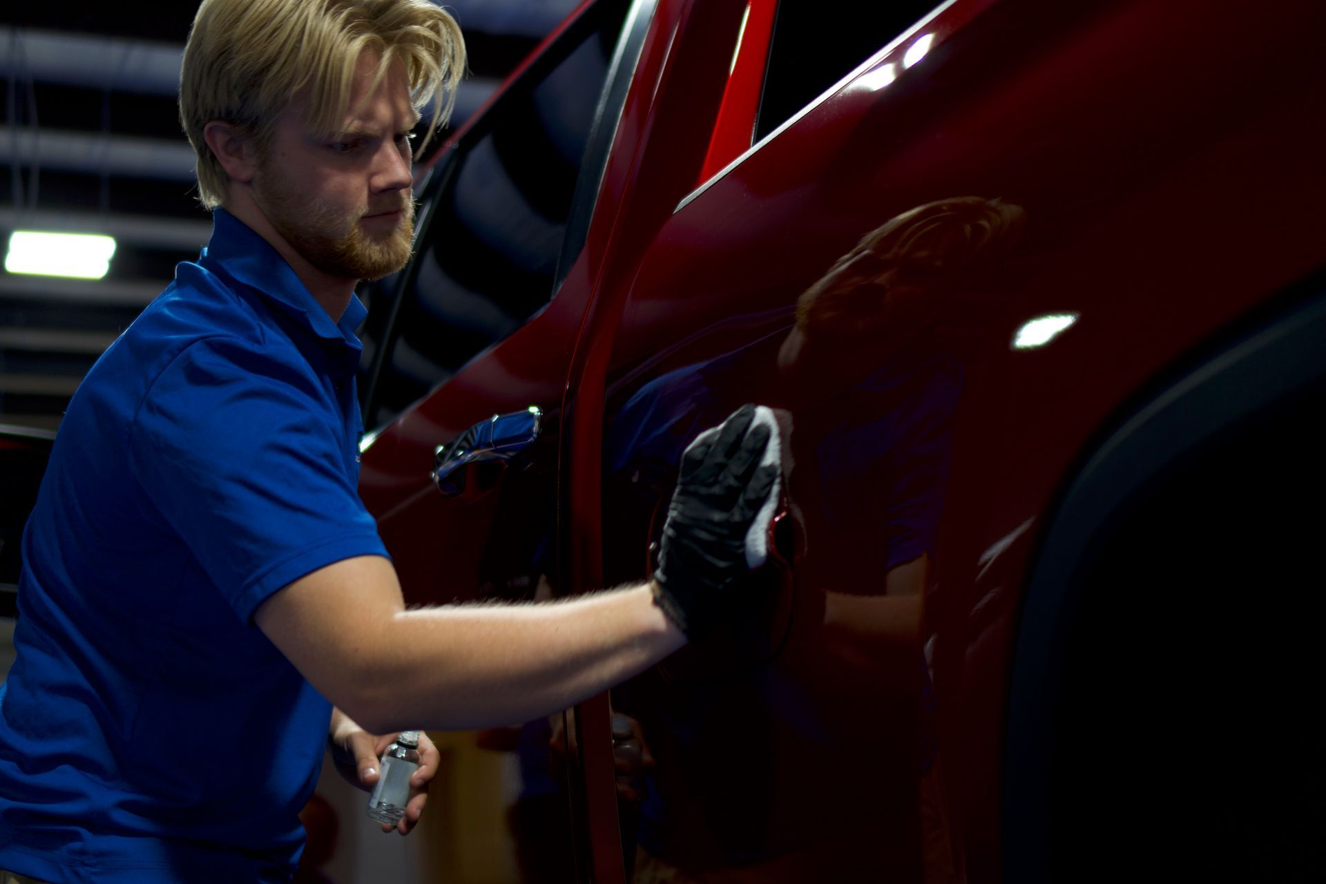 A man is cleaning a car with a cloth in a garage.