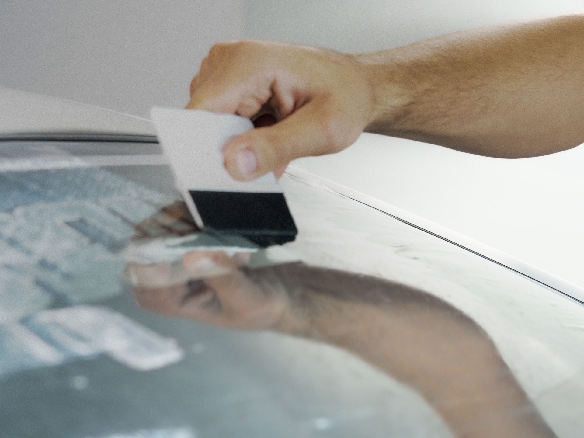 A person's hand using a squeegee to apply a film to a shiny surface.