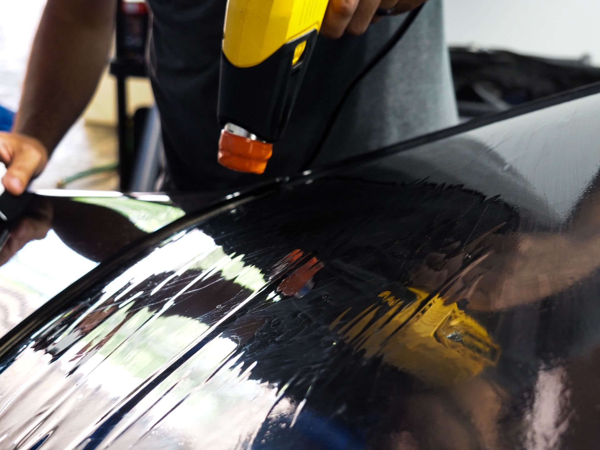 Person using a heat gun on car window tint, in a brightly lit garage.