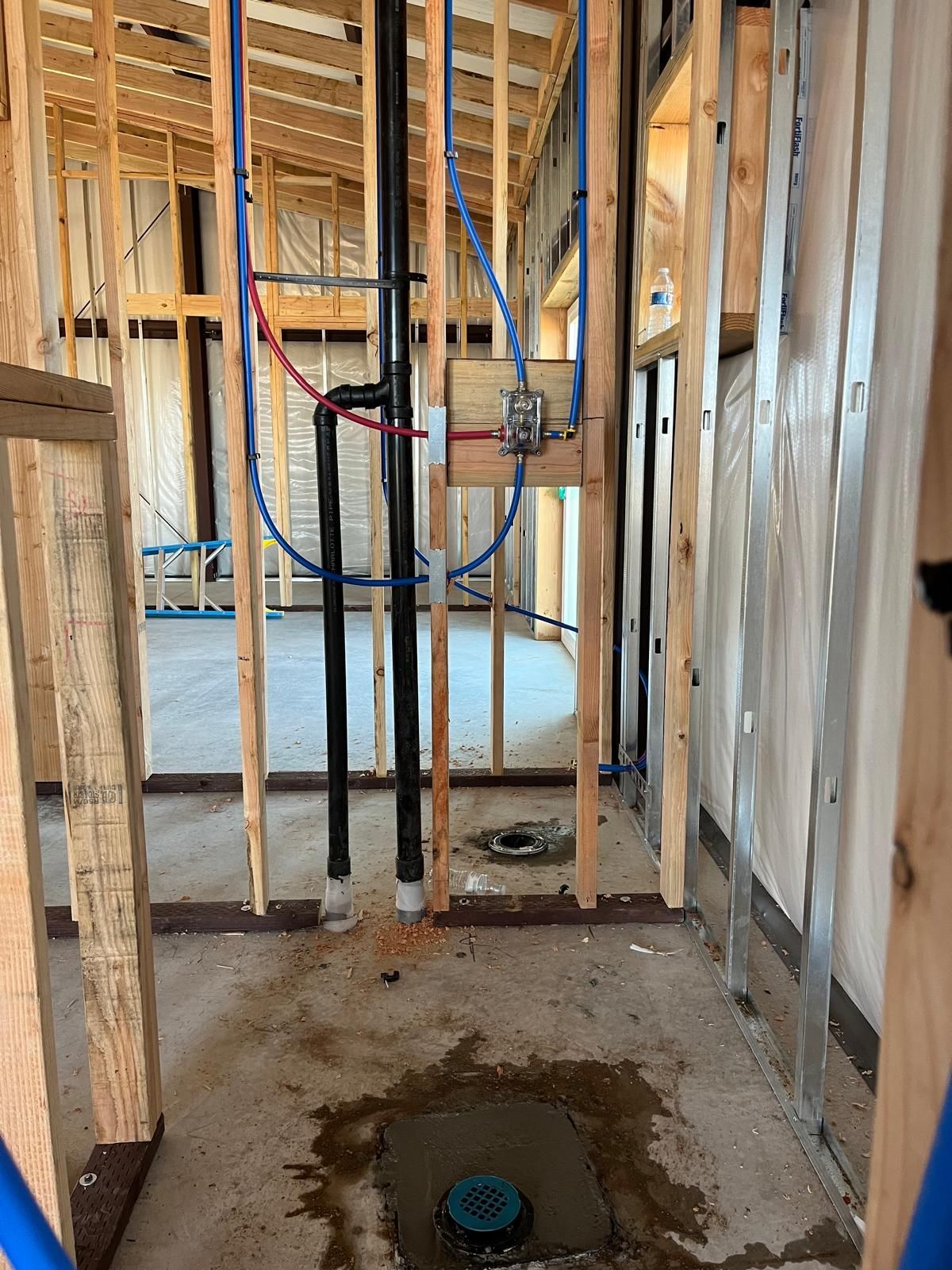 Bathroom under construction with exposed plumbing and framing; concrete floor, pipes in the walls, wood studs.