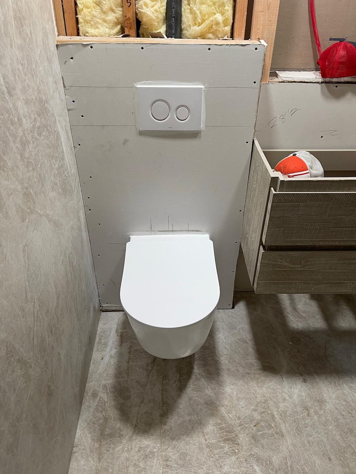 Wall-mounted toilet with dual flush buttons, installed within a partially constructed bathroom.
