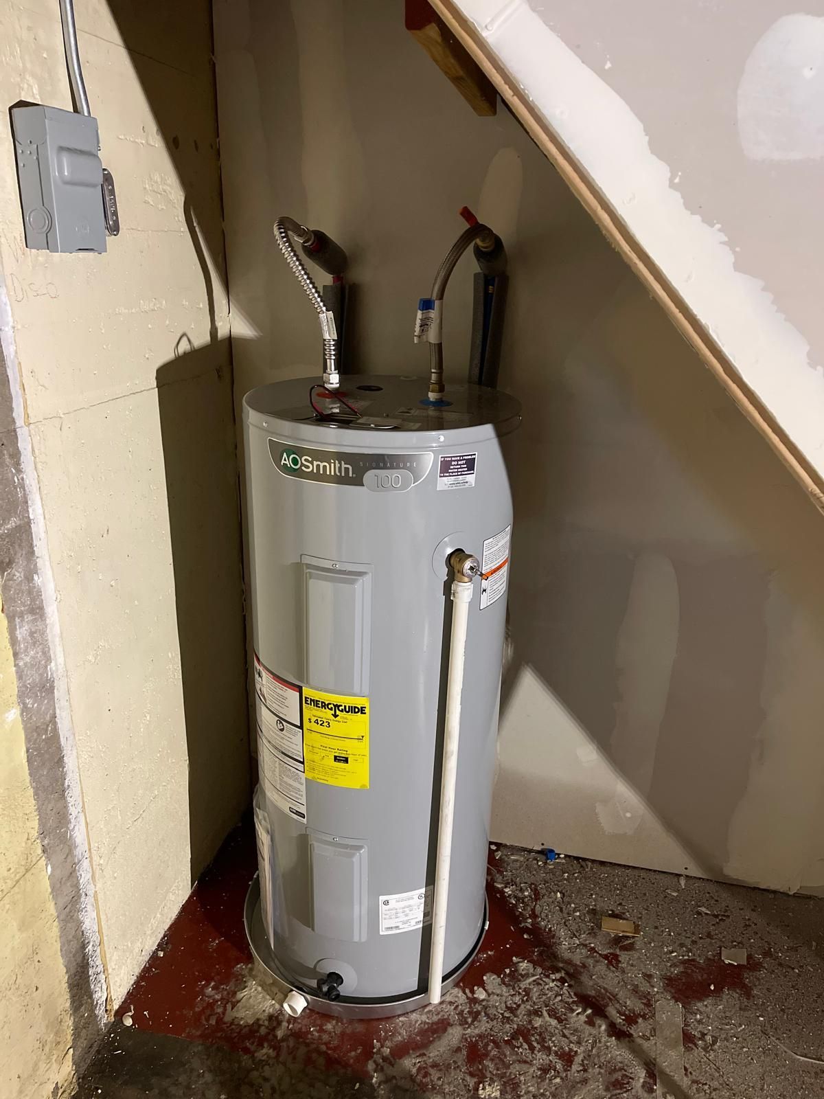 Gray A. O. Smith water heater in a basement corner, with pipes and electrical box visible.