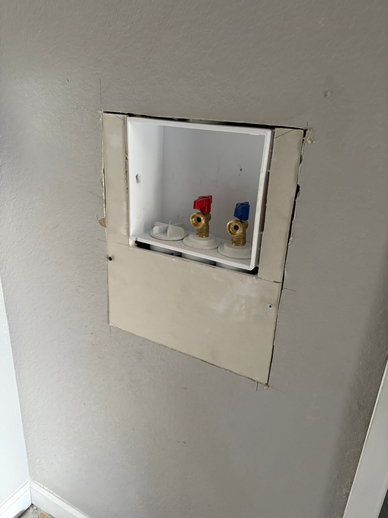 Laundry hookup box on a gray wall with hot/cold water valves; white box with drywall partially attached.