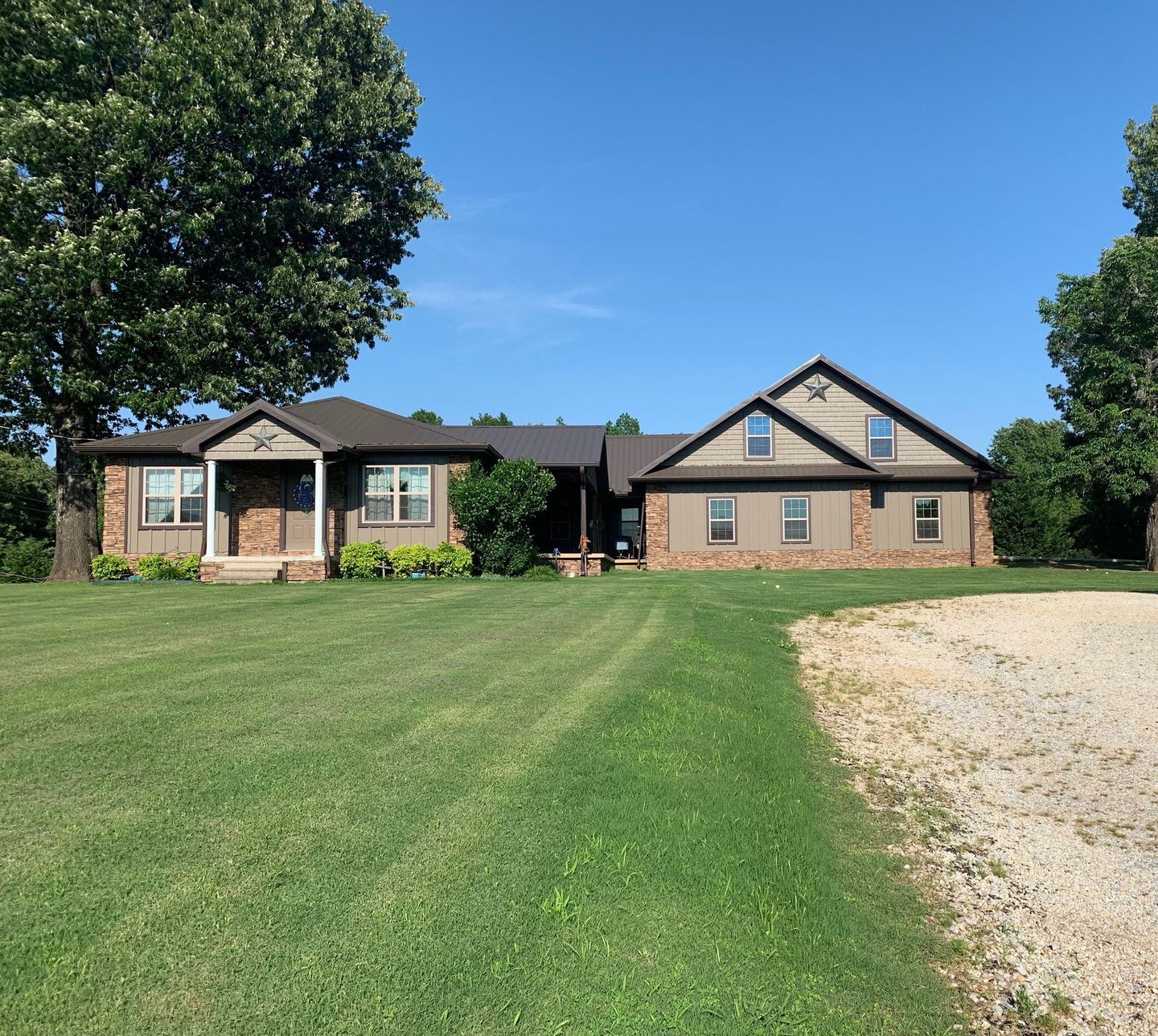 Single-story house with brick facade, front lawn, and gravel driveway under a clear blue sky