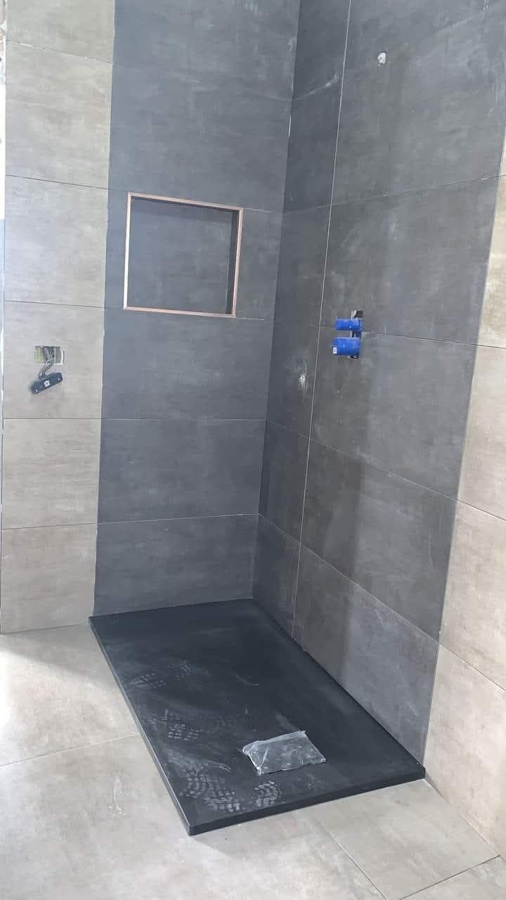 Un box doccia moderno con piastrelle color antracite alle pareti, un piatto doccia scuro abbinato e una nicchia a muro integrata.