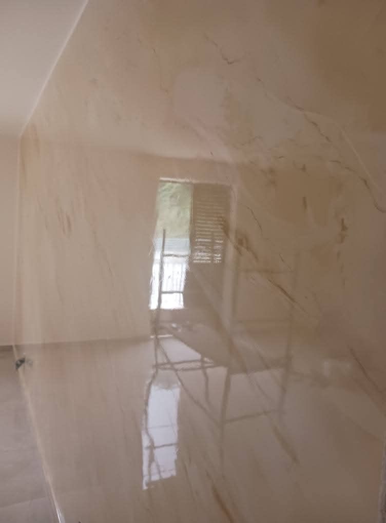 Una parete lucida color beige chiaro con sottili venature marmorizzate riflette la luce e la struttura di un'impalcatura.