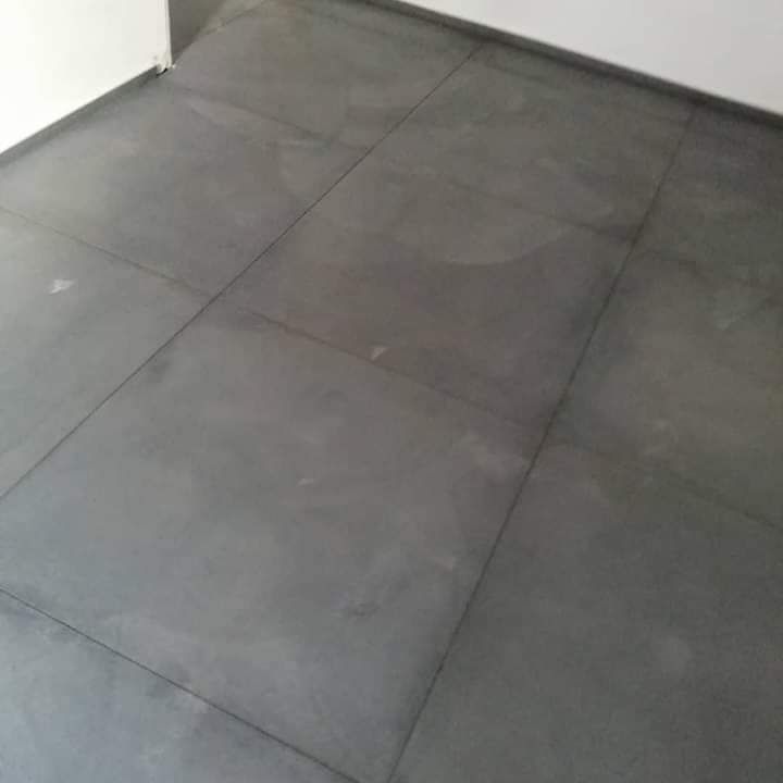 Una ripresa ravvicinata dall'alto di piastrelle quadrate grigio scuro, con fughe visibili, che si uniscono a una parete bianca.