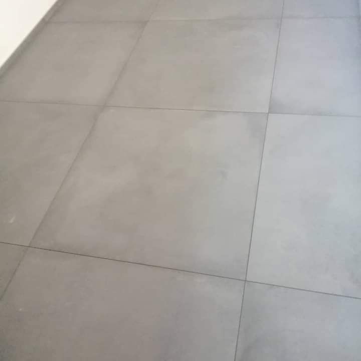 Grandi piastrelle quadrate, grigio chiaro opaco, disposte a griglia con sottili fughe scure.