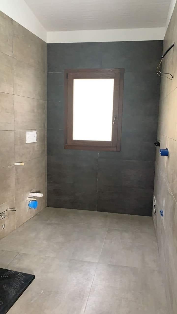 Un bagno non rifinito con pareti e pavimento grigio chiaro, caratterizzato da una parete scura a contrasto con una finestra centrale.