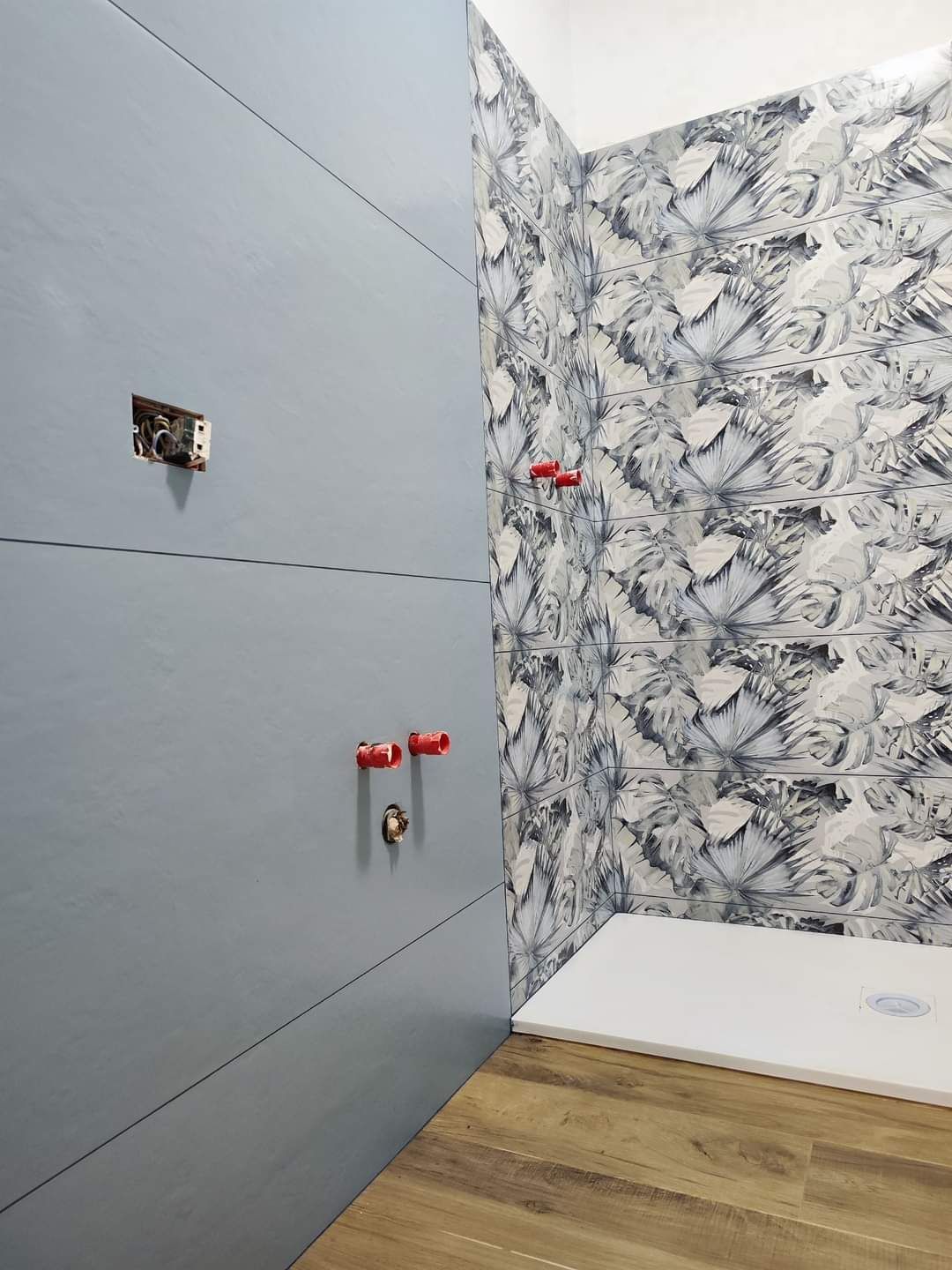 Un bagno moderno in fase di ristrutturazione, caratterizzato da grandi piastrelle a parete grigio-blu, piastrelle decorative decorate e un piatto doccia.