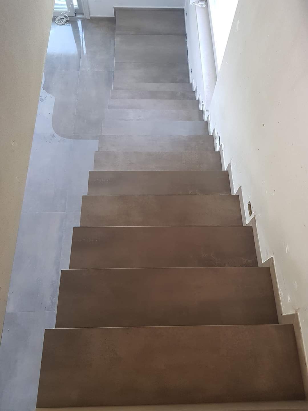 Una scala interna dritta con gradini in legno marrone e pareti rivestite con piastrelle grigio chiaro, in un ambiente minimalista.