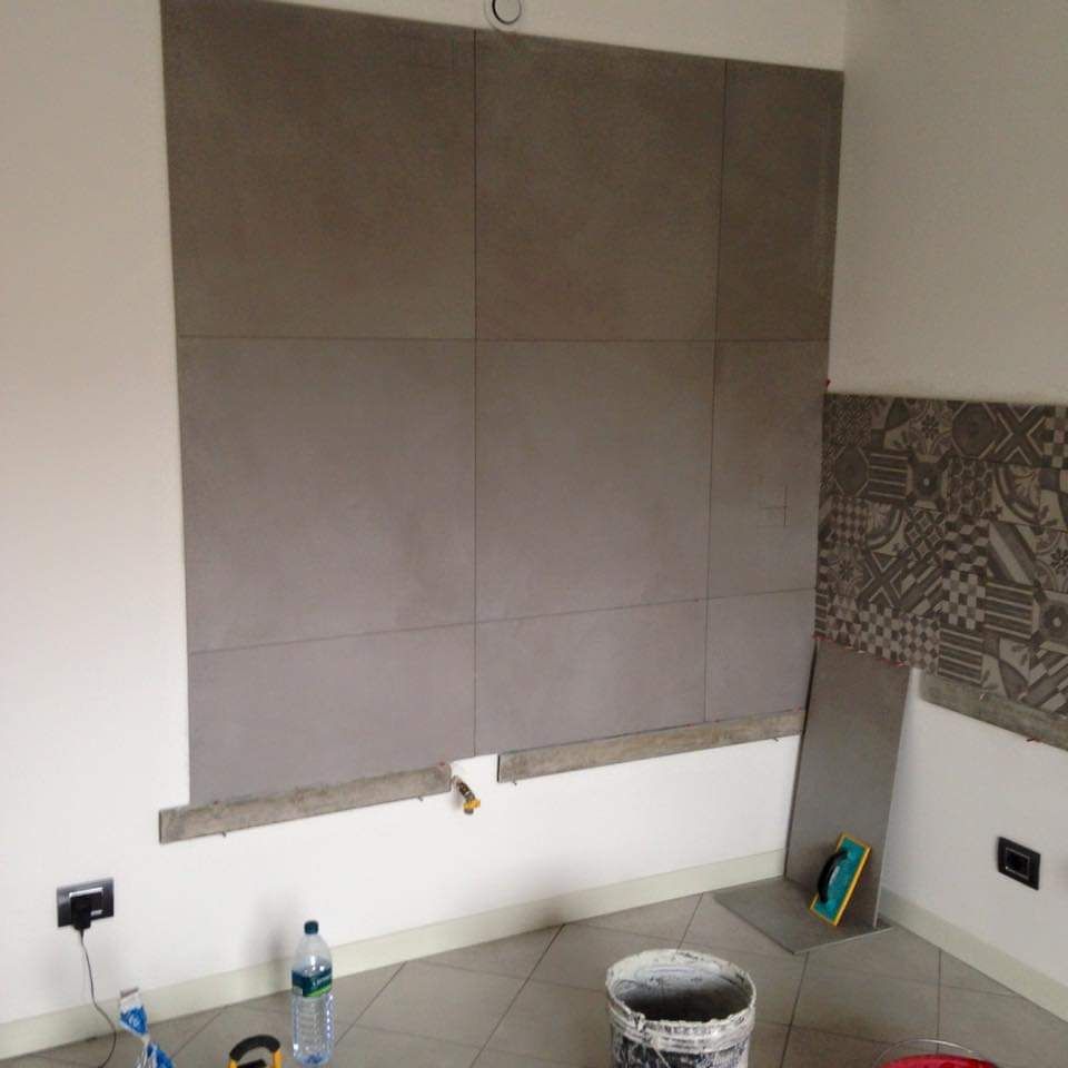 Nell'ambito di una ristrutturazione, su una parete sono state posate grandi piastrelle quadrate grigie, con una piccola sezione di piastrelle decorate su un lato.