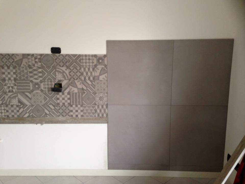 Una parete bianca con una sezione di piastrelle grigie decorate sulla sinistra e quattro grandi piastrelle quadrate grigie a tinta unita sulla destra.