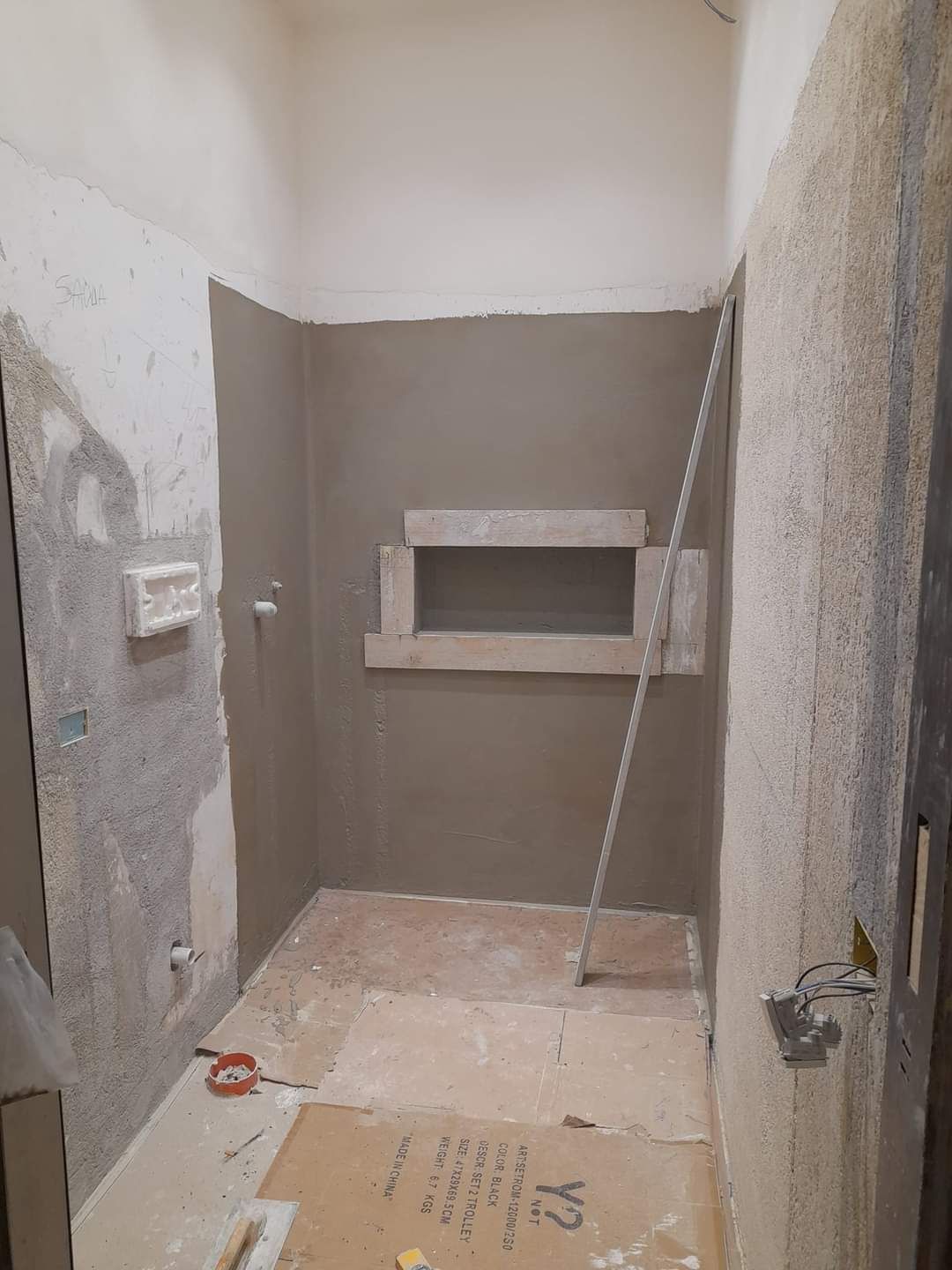 Una stanza interna non rifinita con pareti intonacate di grigio, una nicchia rettangolare a muro e detriti edili sul pavimento.