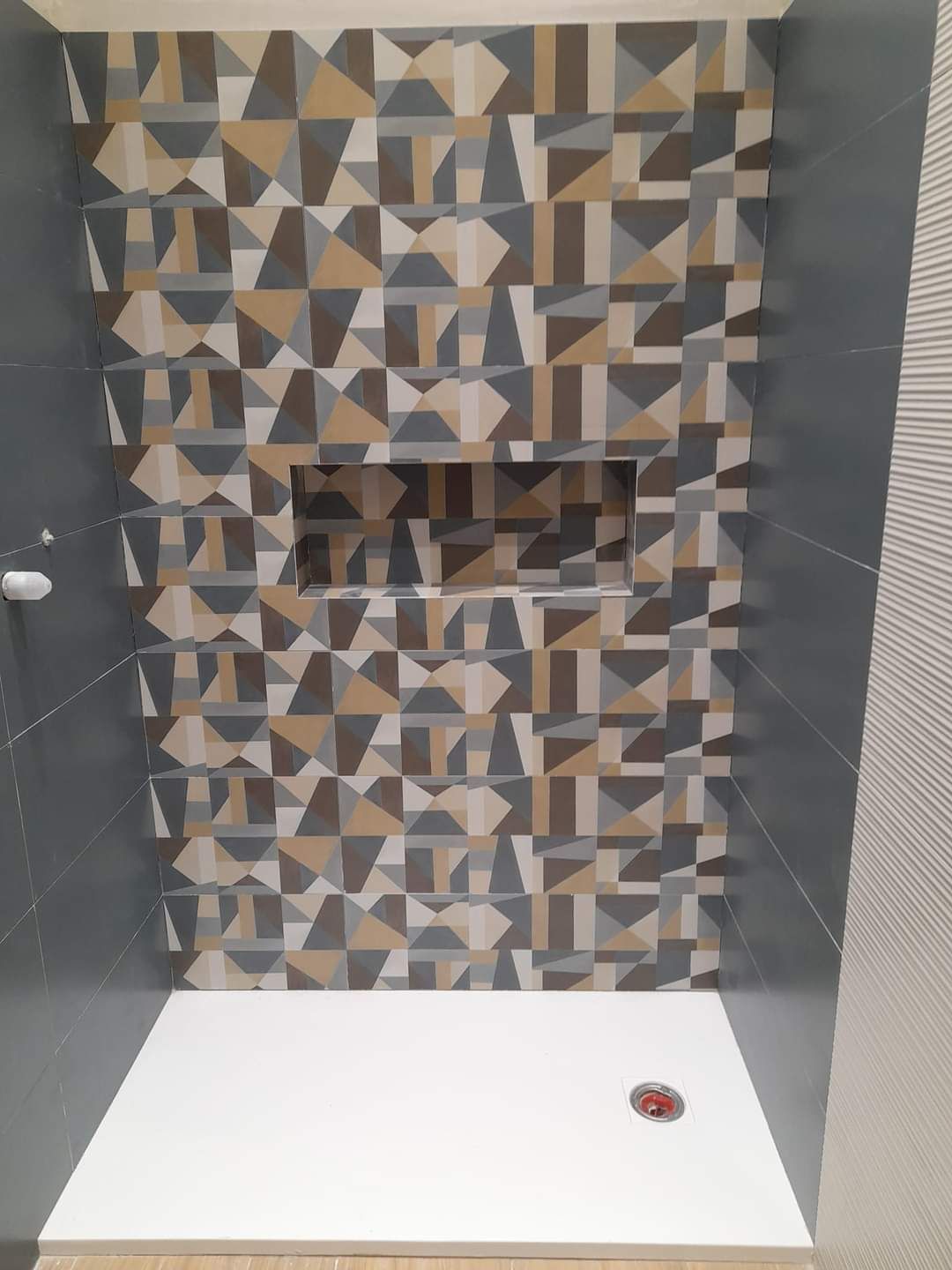 Box doccia con piastrelle geometriche decorate nei toni del marrone, grigio e bianco, caratterizzato da una nicchia centrale incassata nella parete.