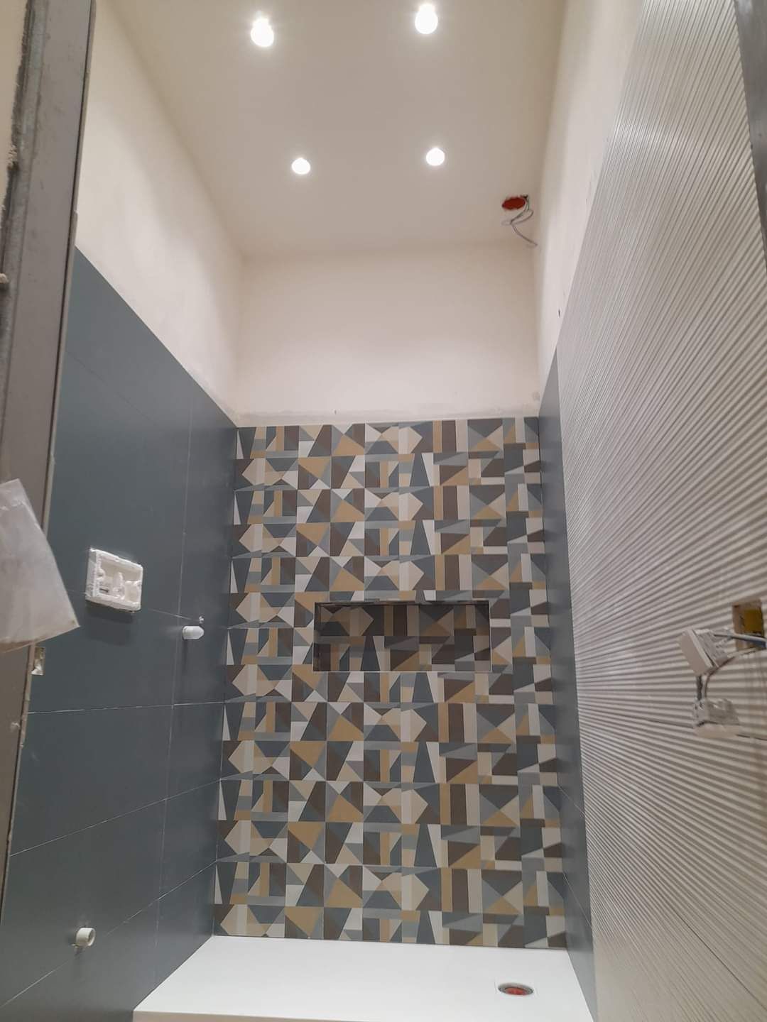 Un box doccia moderno con pareti grigio scuro, una parete decorativa rivestita con piastrelle geometriche decorate e un pavimento bianco.