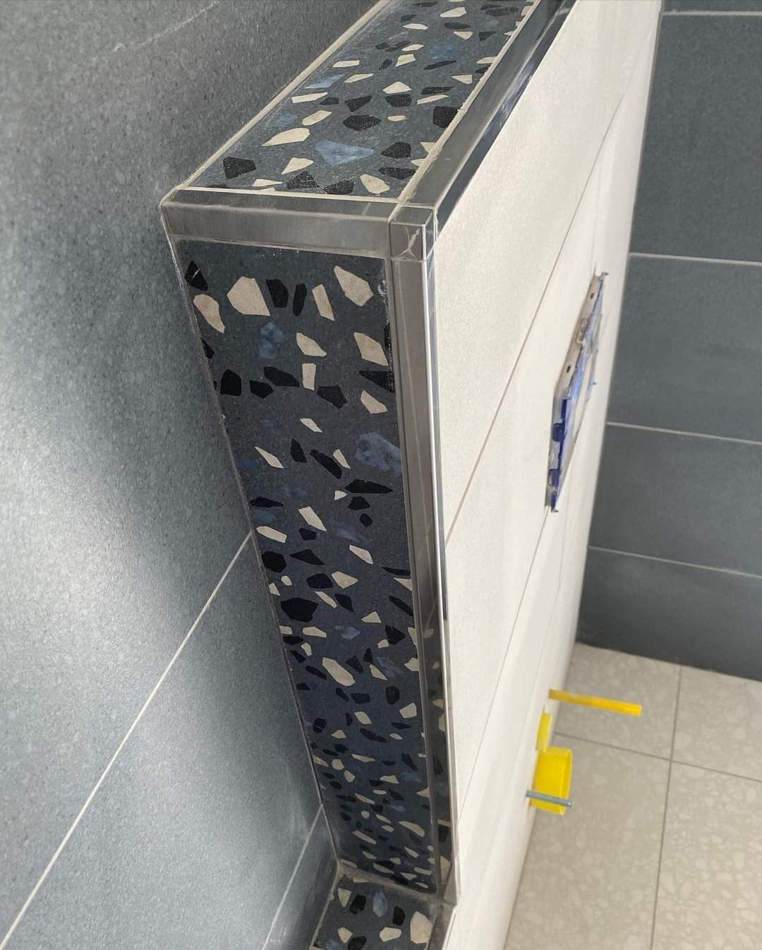 Installazione moderna di un WC sospeso con dettagli in terrazzo grigio e profili angolari metallici in un bagno piastrellato.