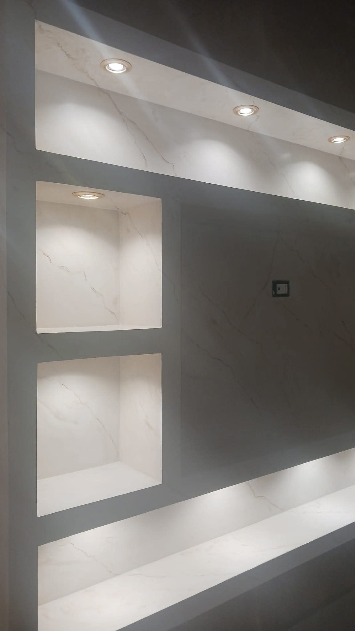 Un moderno mobile a parete con ripiani incassati, faretti integrati e dettagli con motivo effetto marmo bianco.