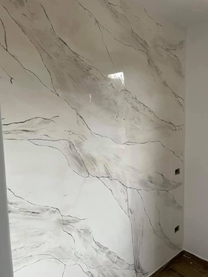 Una parete rivestita con intonaco bianco effetto marmo, caratterizzato da sottili venature grigio scuro e una finitura liscia e lucida.