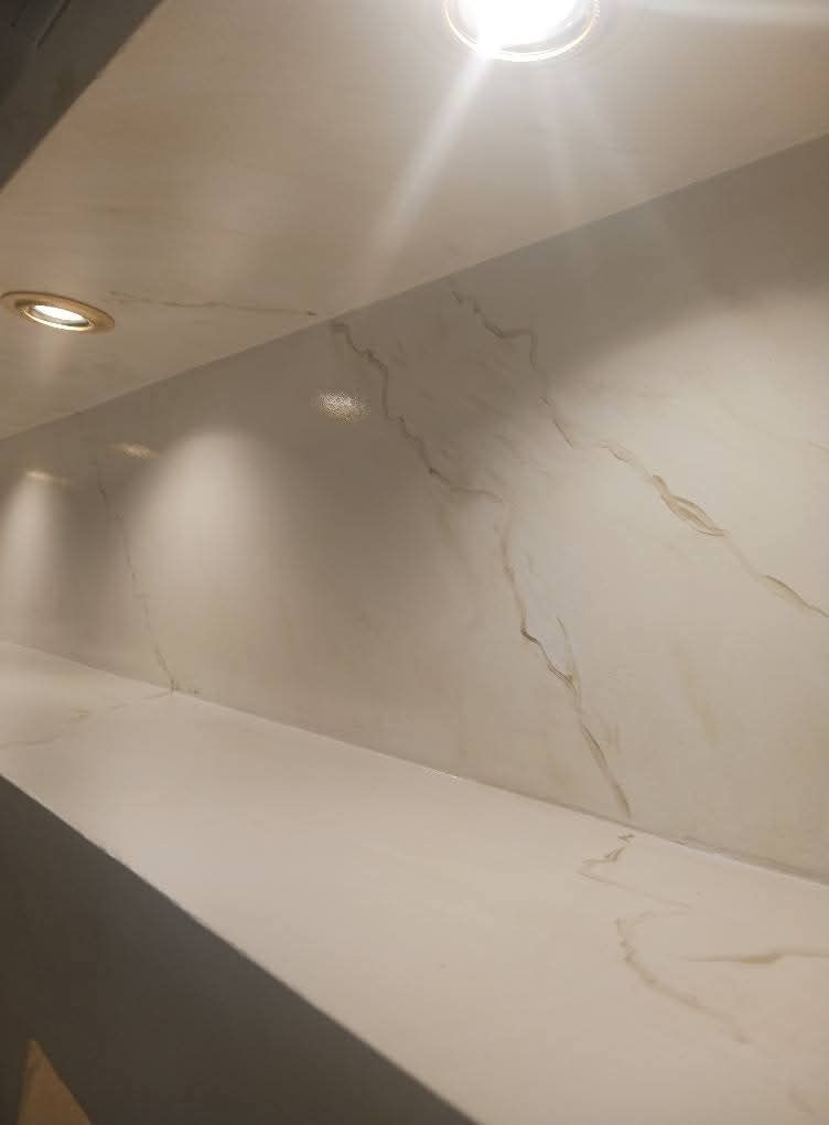 Piano di lavoro e paraschizzi in marmo bianco con delicate venature grigie e dorate, illuminati da faretti a incasso a soffitto.