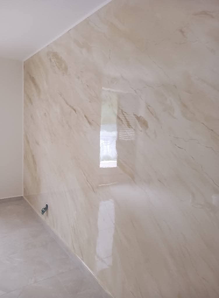 Una parete liscia e levigata con motivi marmorizzati beige e crema, che riflette la luce in una stanza minimalista e moderna.