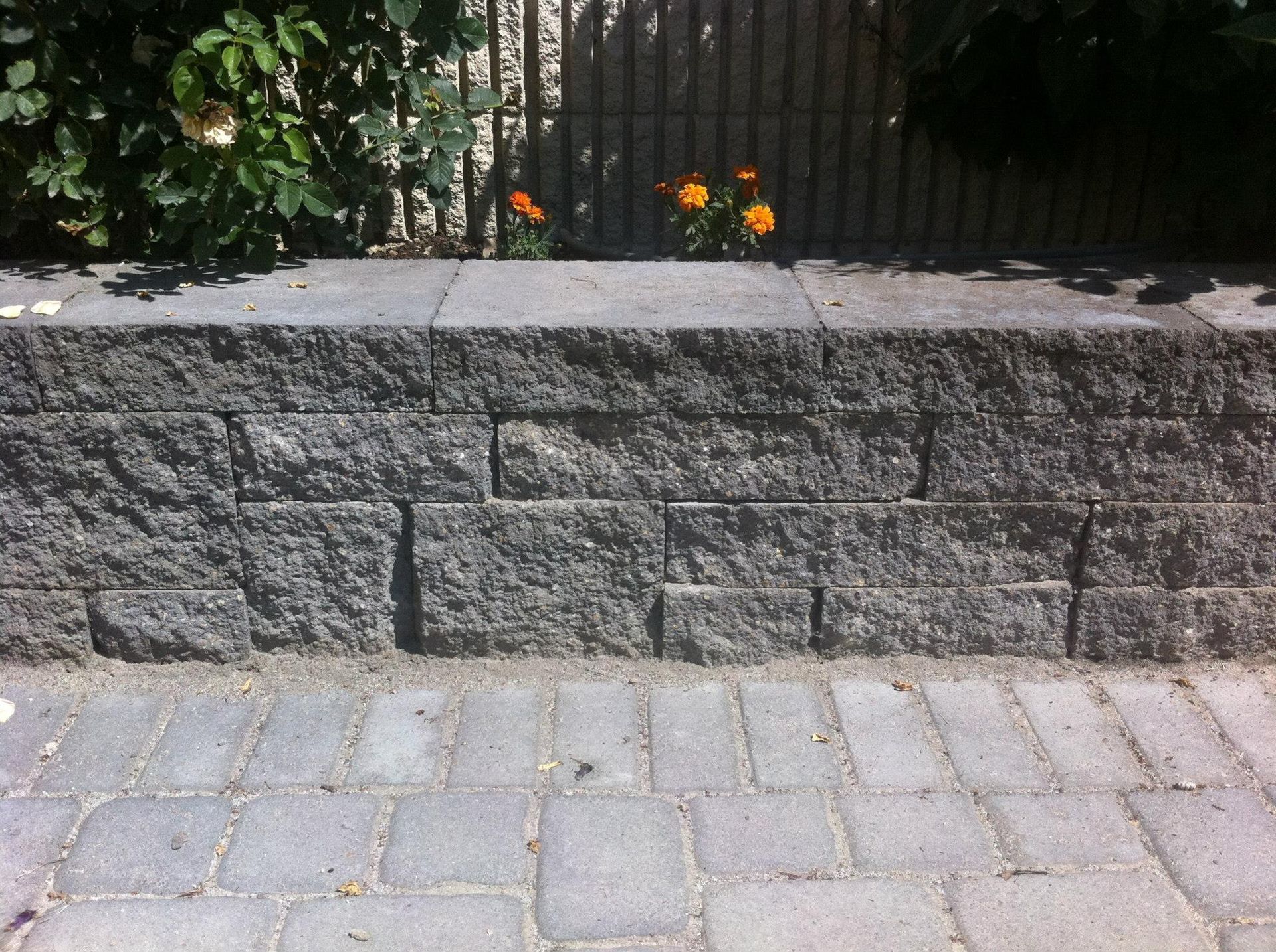 A low garden retaining wall made of stacked gray textured concrete blocks bordering a stone-paved patio.