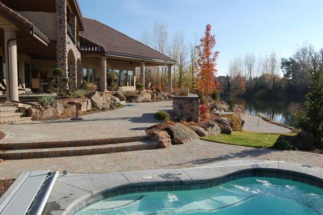 A view of a stone patio with steps, a house, and a pool, overlooking a pond on a sunny day.