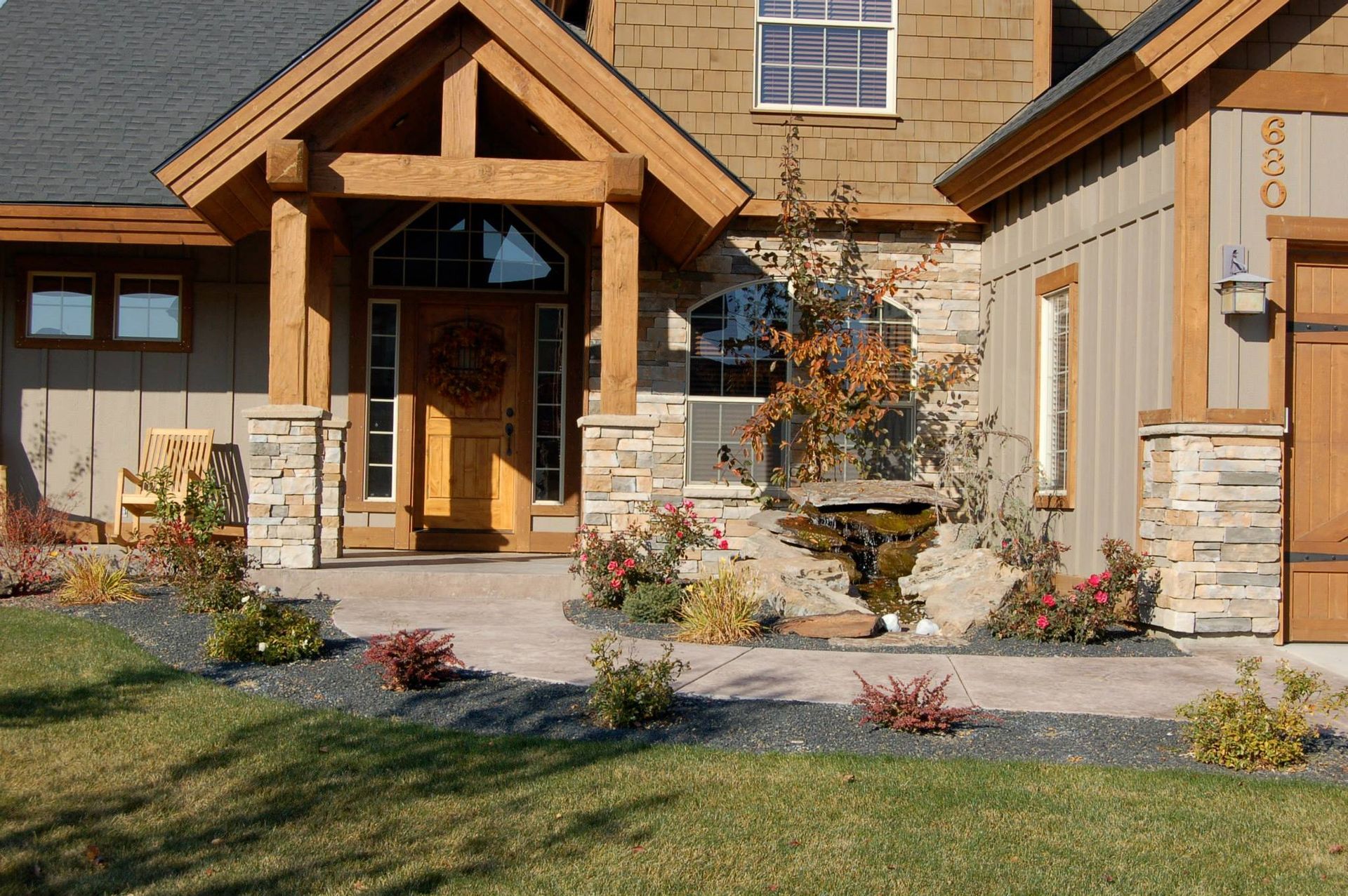 The front entrance of a modern rustic-style home with timber framing, stone accents, and a paved walkway.