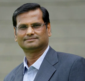 A man in a suit and glasses looks at the camera