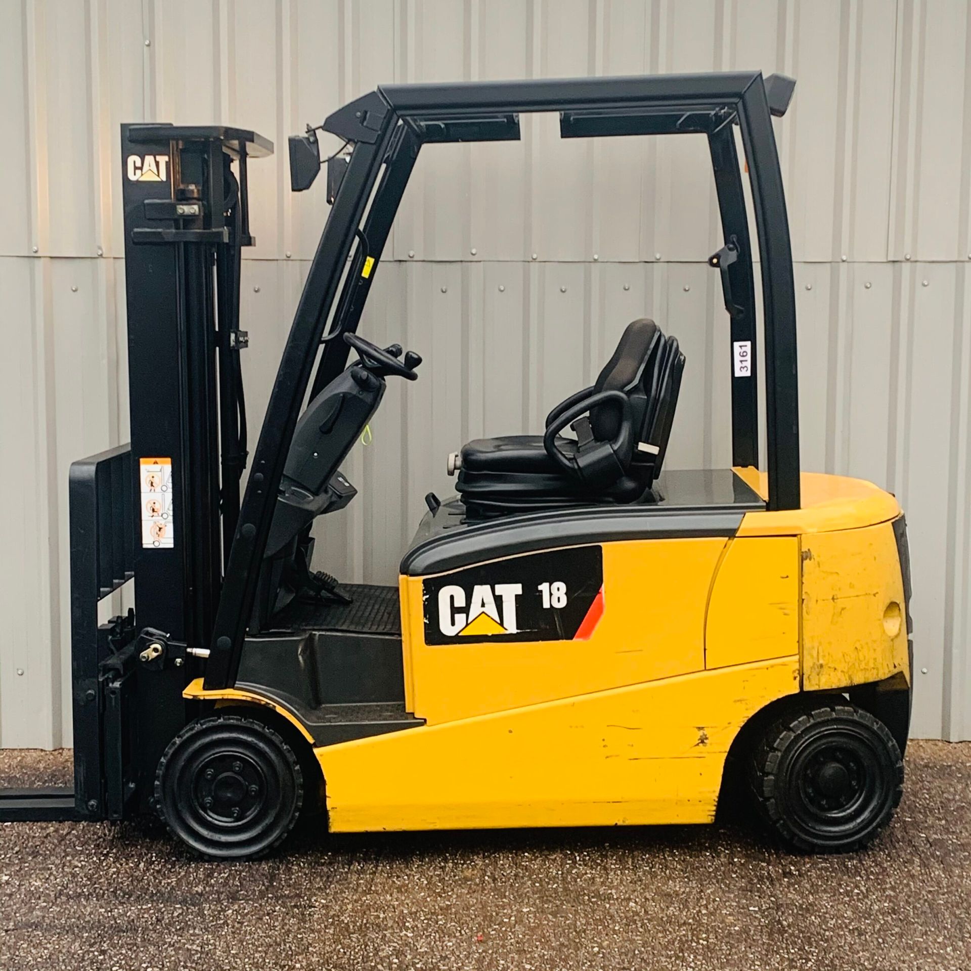 A yellow cat 18 forklift is parked in front of a building