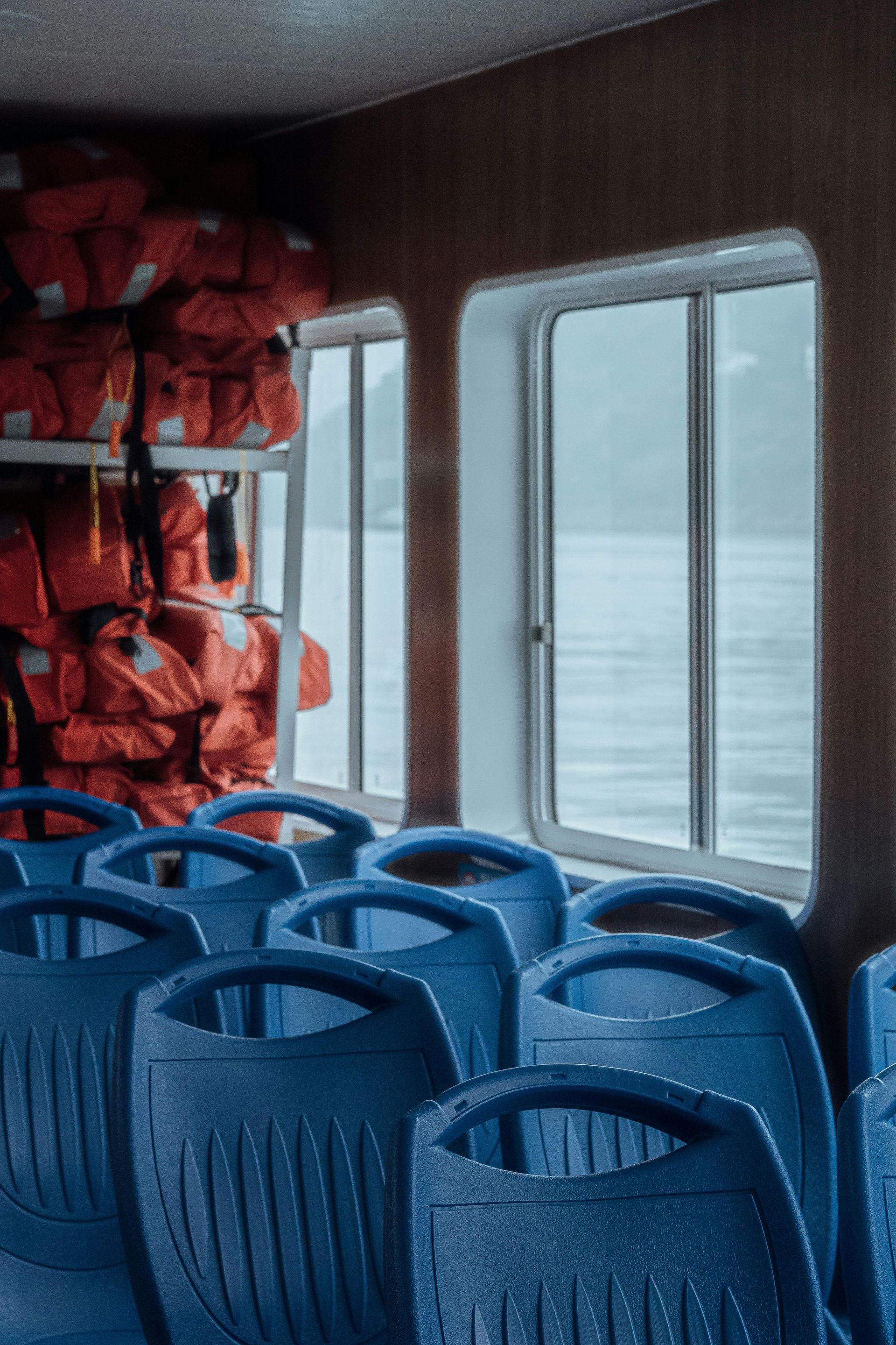 A row of blue seats on a boat next to a window.