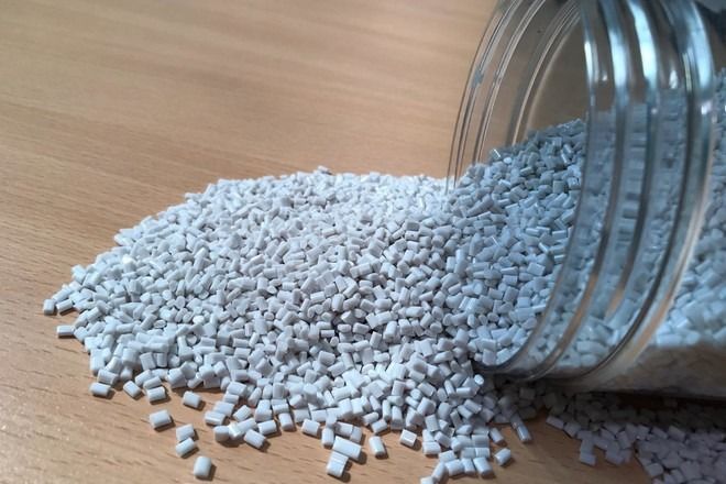 A glass jar filled with white plastic granules on a wooden table.